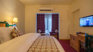 Una habitación de hotel con una cama, un escritorio, un televisor y un ventanal con cortinas.