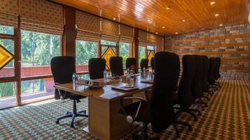 Un salón de conferencias con una larga mesa, numerosas sillas y ventanas amplias con vistas a zonas verdes.