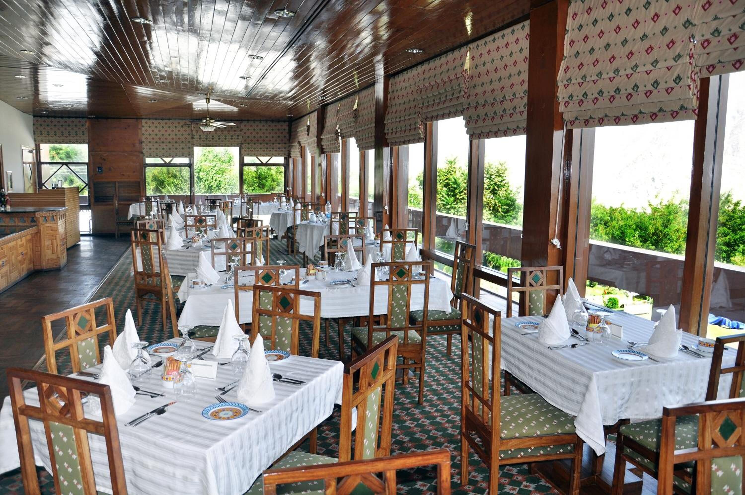 A restaurant with multiple tables set for dining, featuring wooden chairs and white tablecloths.