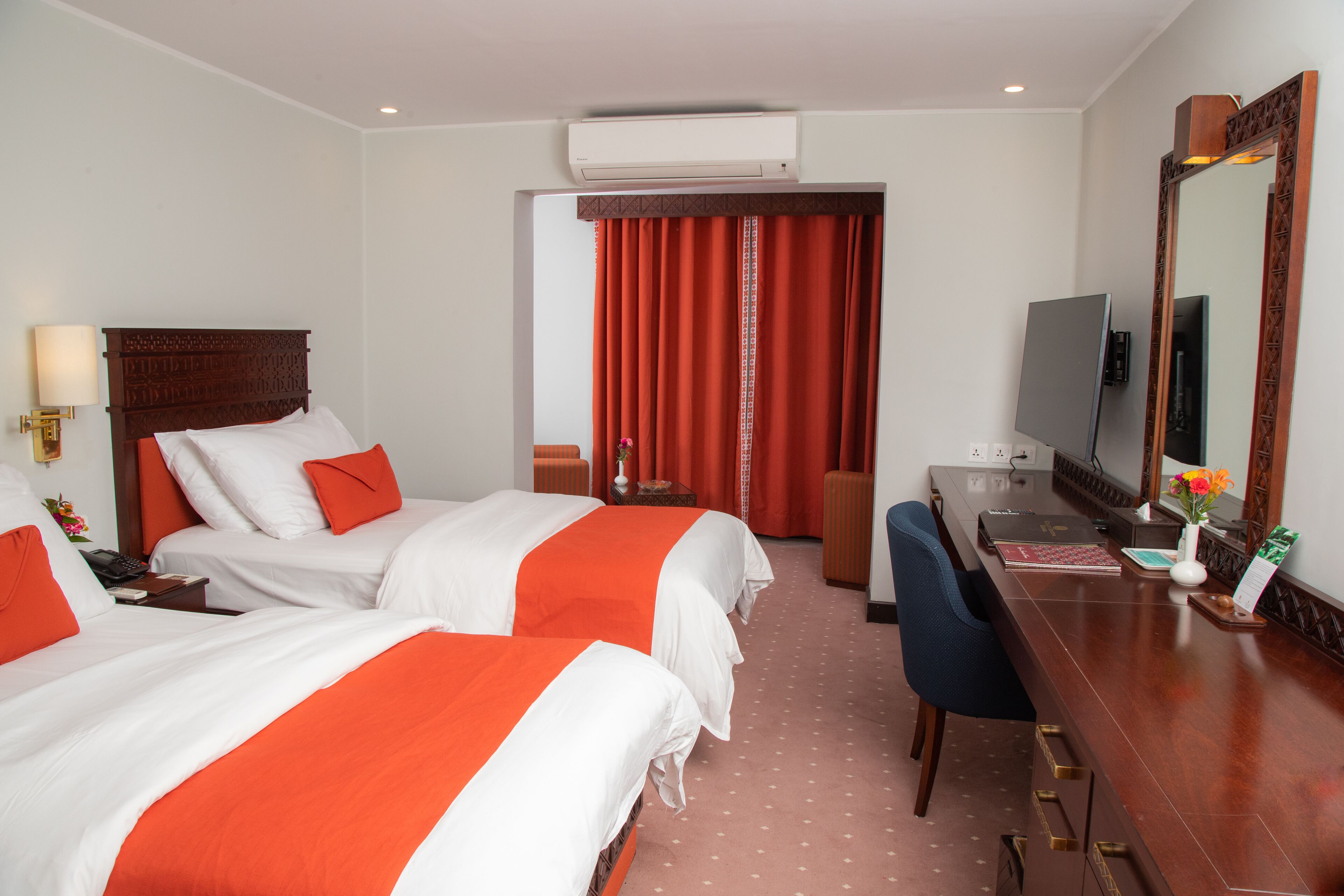 Habitación de hotel con dos camas, un escritorio, una silla, un televisor y aire acondicionado.