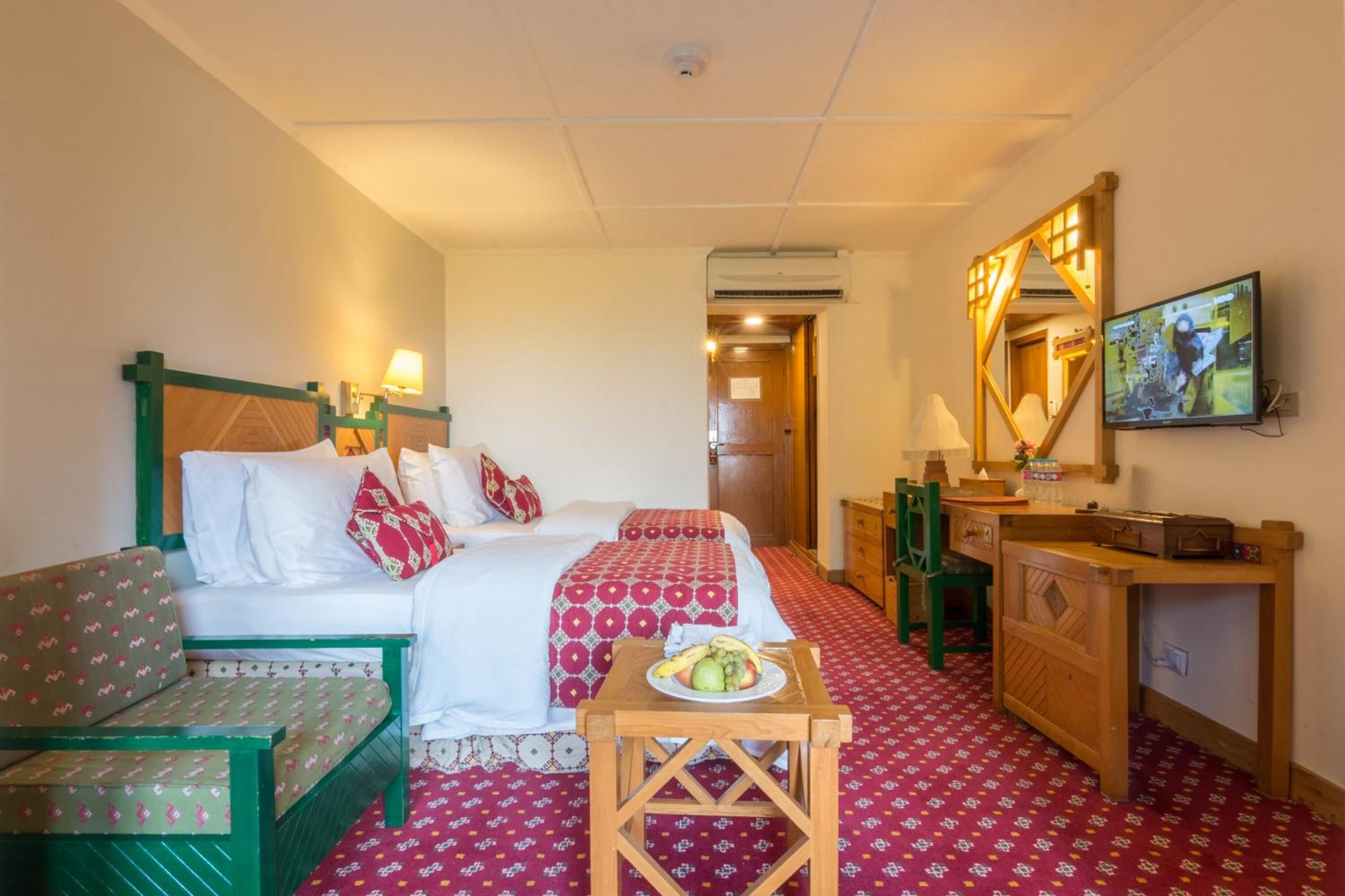 Une chambre d’hôtel avec un lit, un canapé, une petite table avec des fruits, un bureau, un miroir et une télévision.