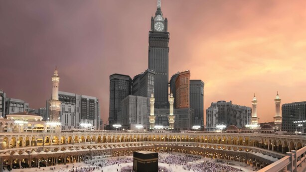 Una gran mezquita con un minarete destacado y una torre de reloj, rodeada de edificios modernos.