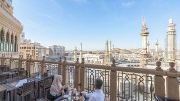 Comedor con mesas y sillas, con vistas a un paisaje urbano con edificios y una mezquita.