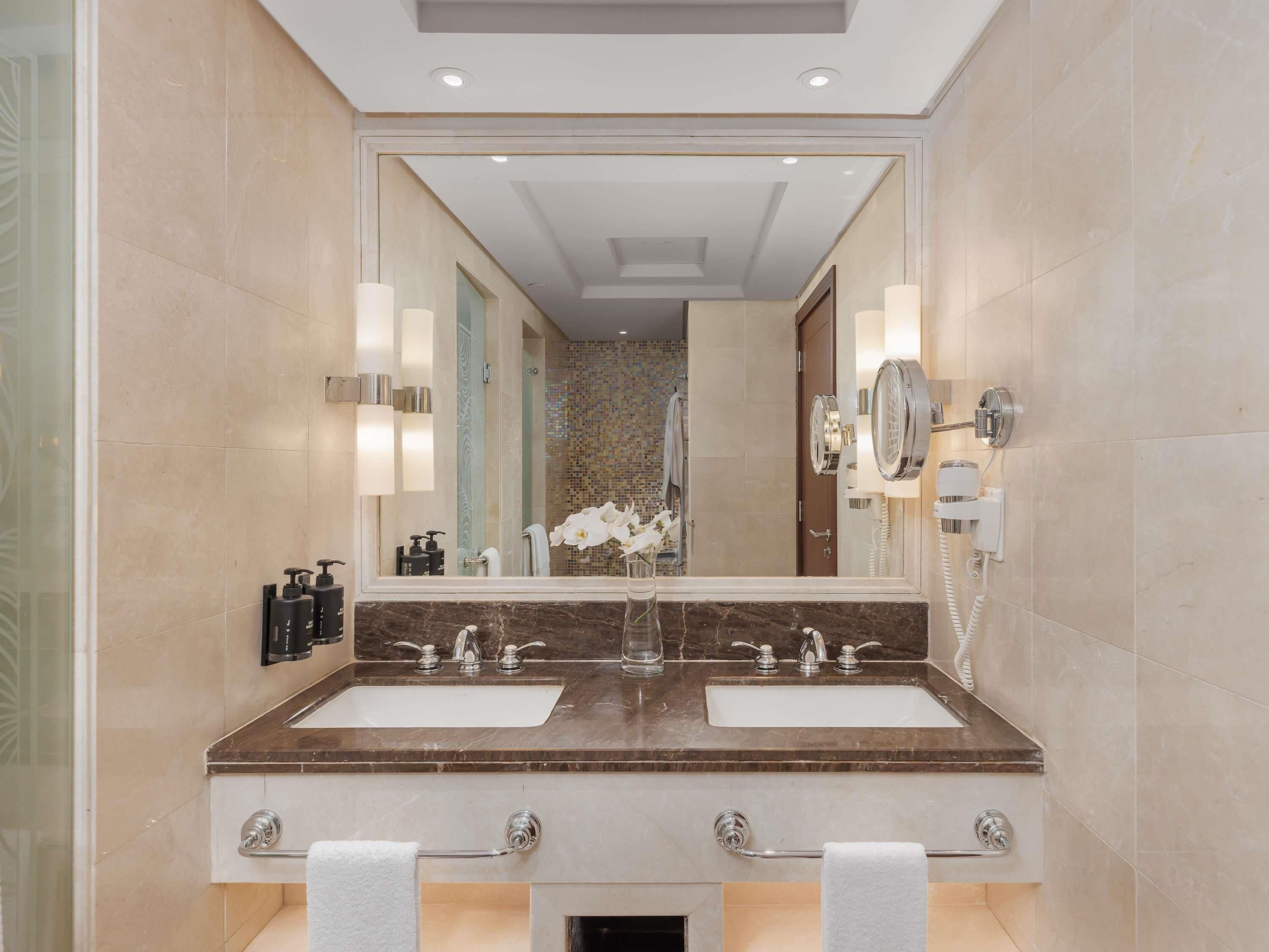 A modern bathroom with two sinks, a large mirror, and a hairdryer.