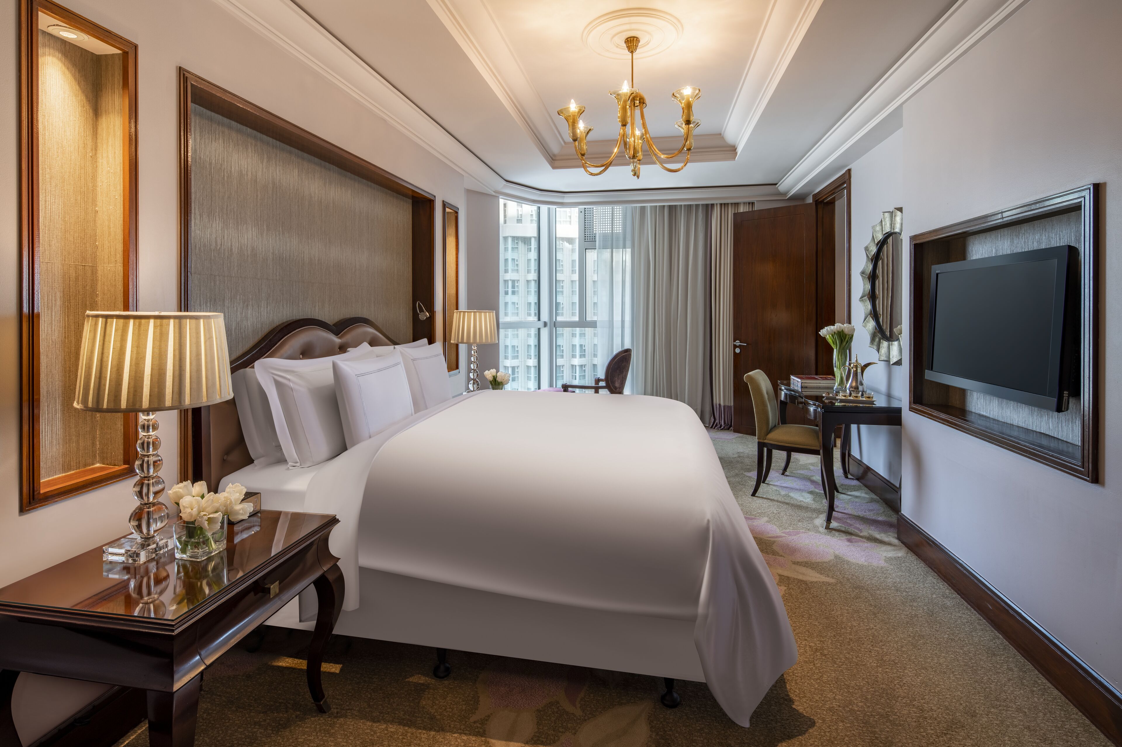 Une chambre d’hôtel avec un grand lit, un bureau avec une lampe, une chaise, une télévision et une vue sur la ville.