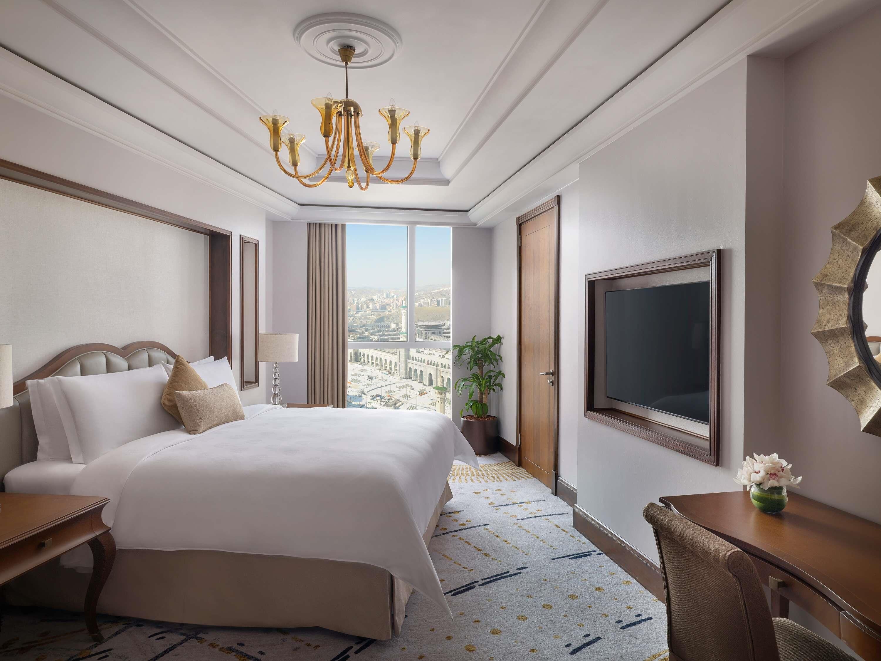 A hotel room with a large bed, a desk, a TV, and a view of the city.