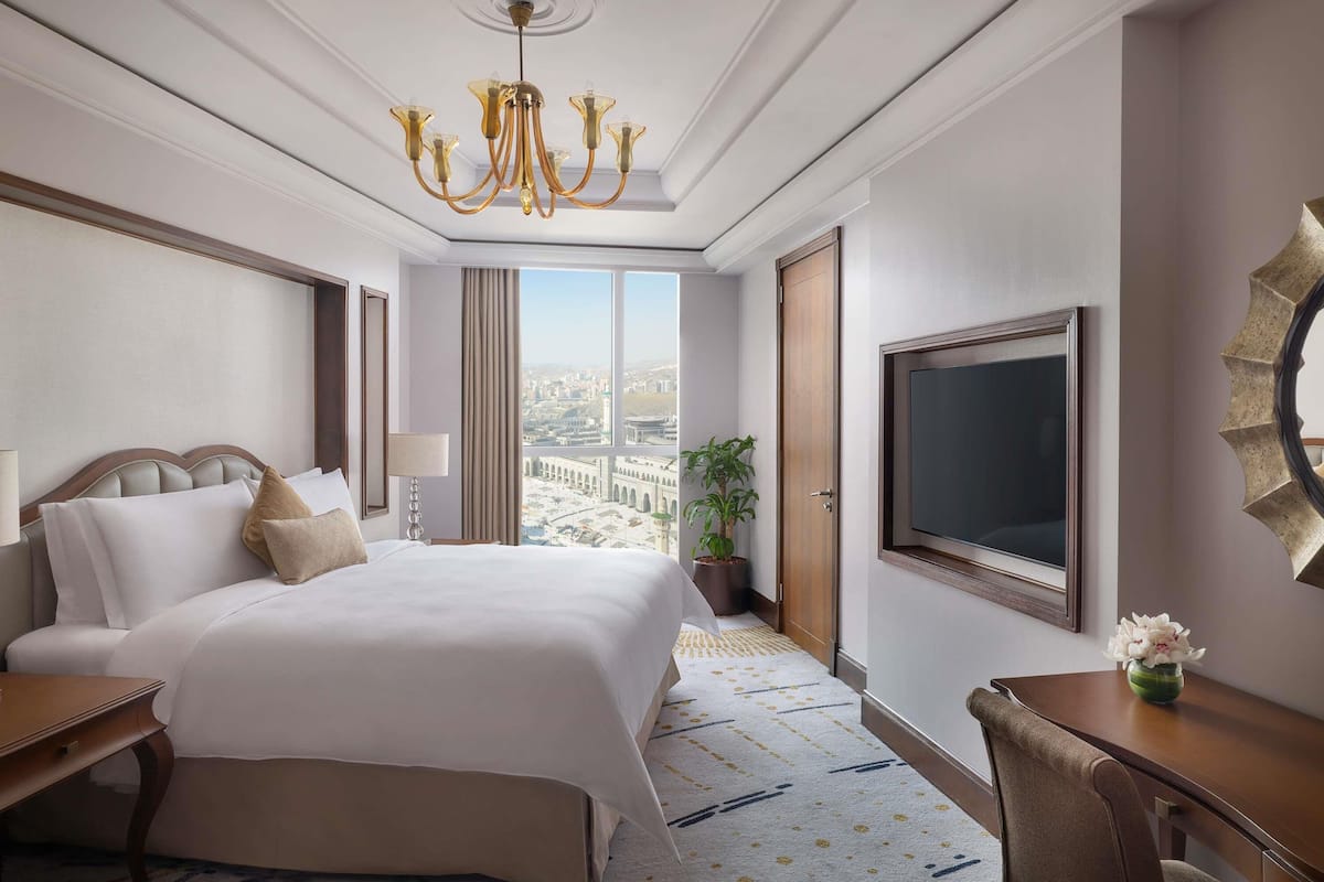 A hotel room with a large bed, a desk, a TV, and a view of the city.