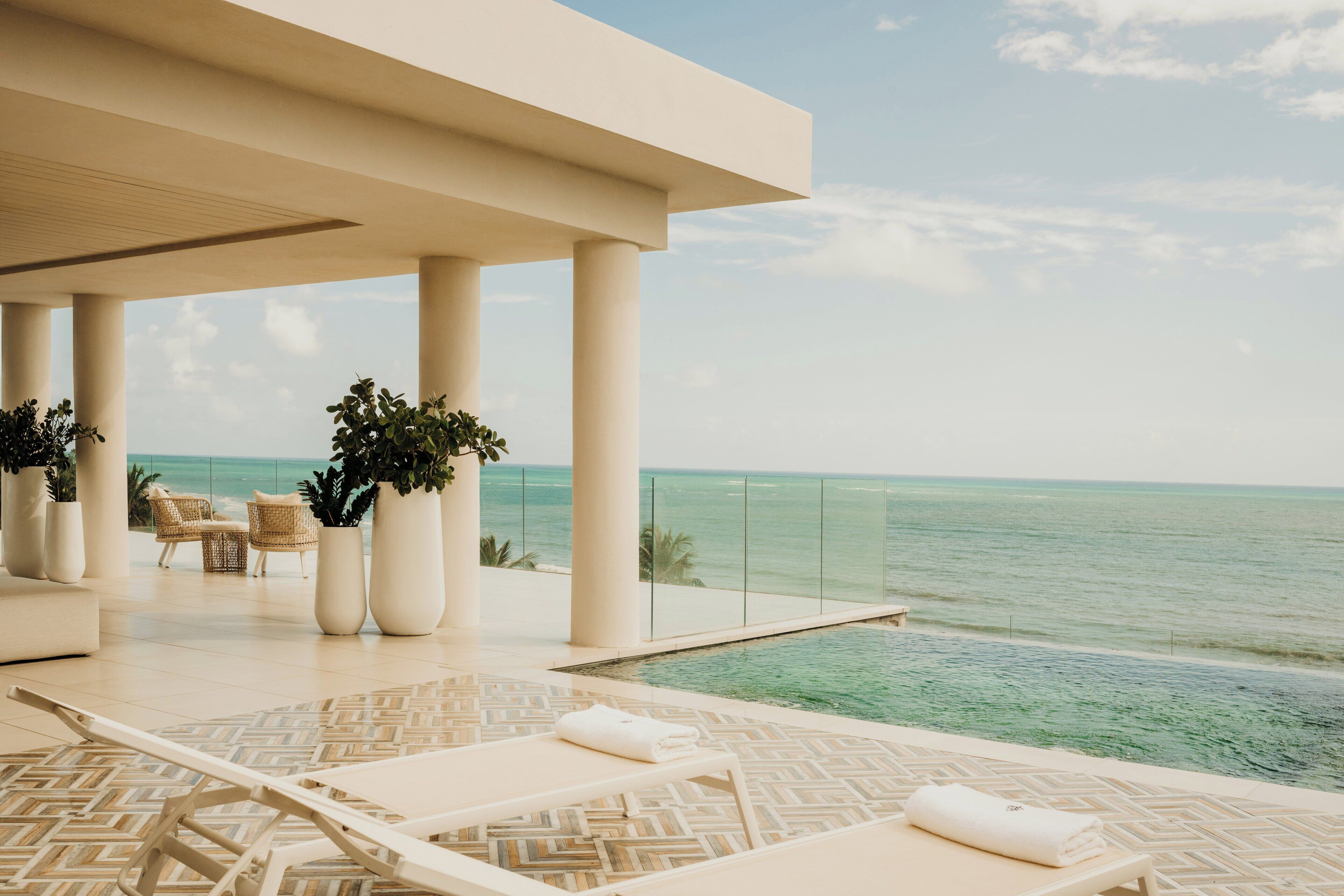 A poolside area with lounge chairs and potted plants, overlooking the ocean.