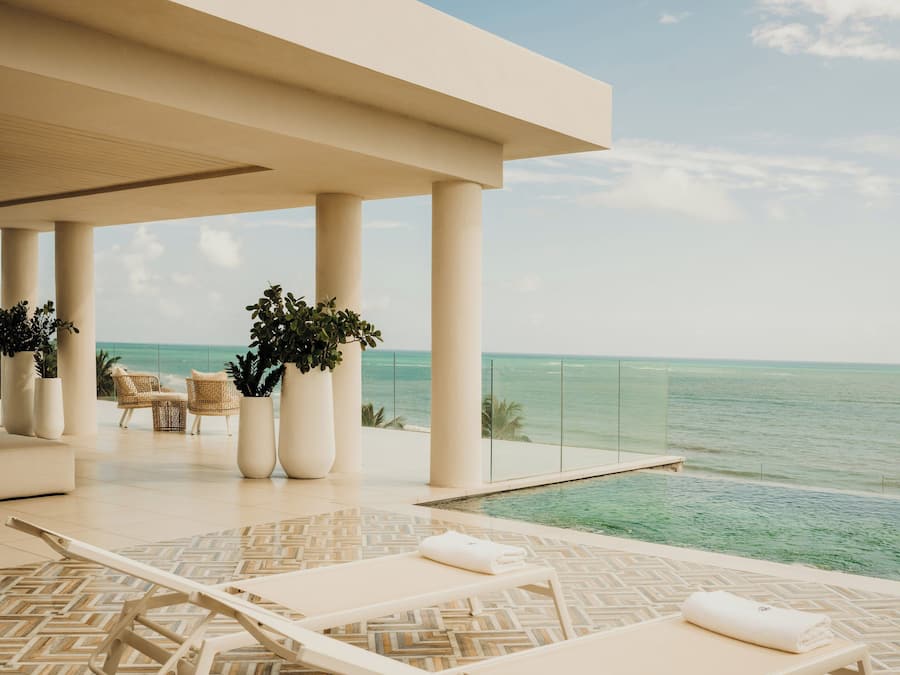A poolside area with lounge chairs and potted plants, overlooking the ocean.