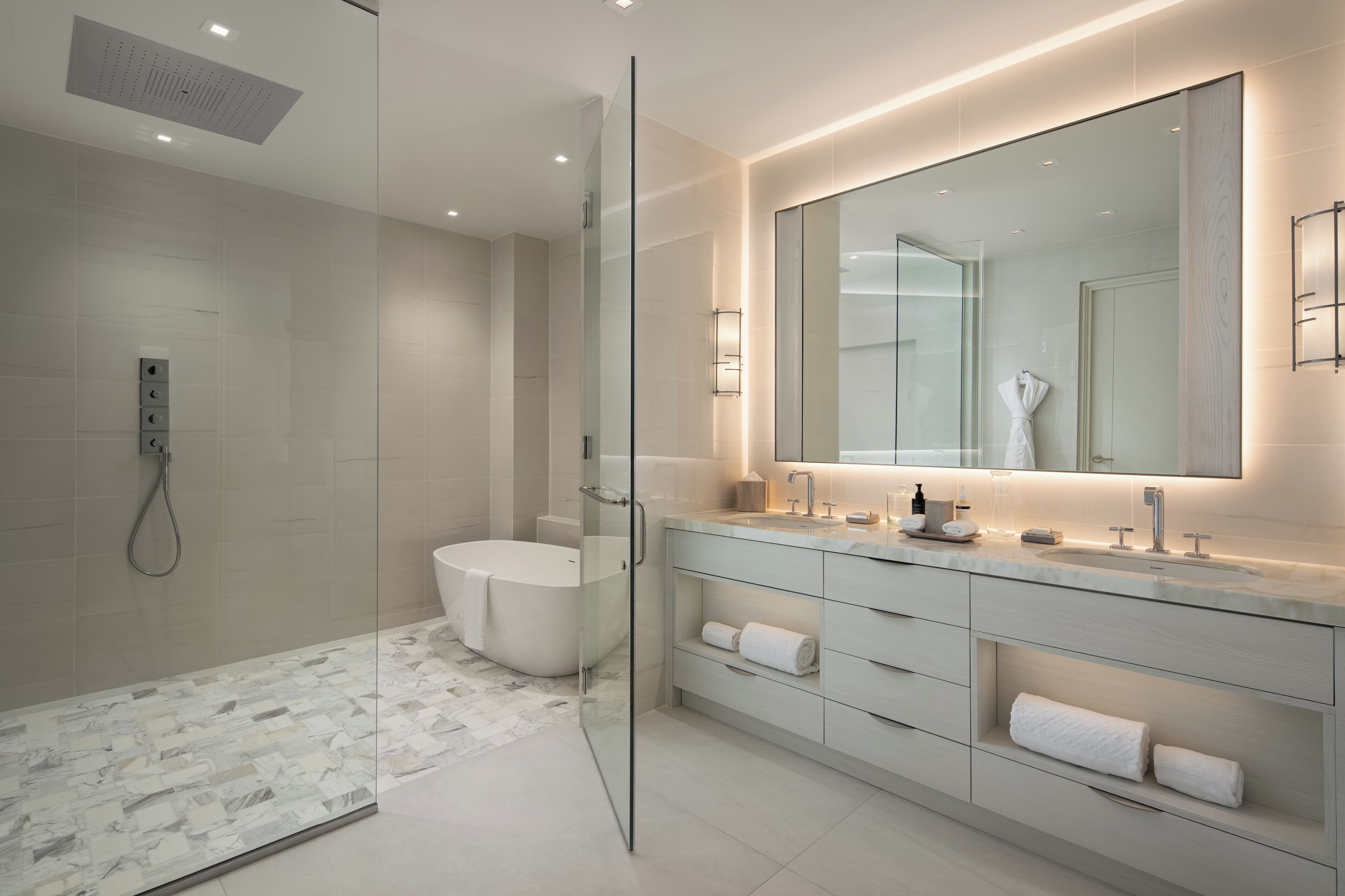 A modern bathroom with a glass-enclosed shower, a freestanding bathtub, and a vanity with a large mirror and built-in shelves.