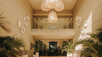 Un vestíbulo espacioso con techo alto, lámparas decorativas en el techo y una escalera central, además de abundante vegetación de interior.