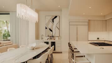 A modern kitchen with a central island, a dining area with a marble table, and a living space with a sofa and curtains.