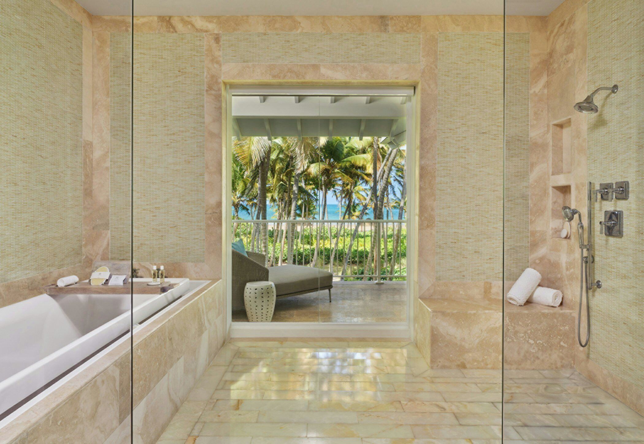 A bathroom with a bathtub, shower, and a view of palm trees and the ocean.