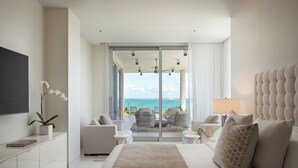 A modern hotel room with a large bed, a flat-screen TV, a sofa, a coffee table, and a balcony with a view of the ocean. - Four Seasons Resort and Residences Puerto Rico (Río Grande)