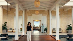 A spacious indoor corridor with a wooden floor, white columns, and hanging pendant lights. - Four Seasons Resort and Residences Puerto Rico (Río Grande)