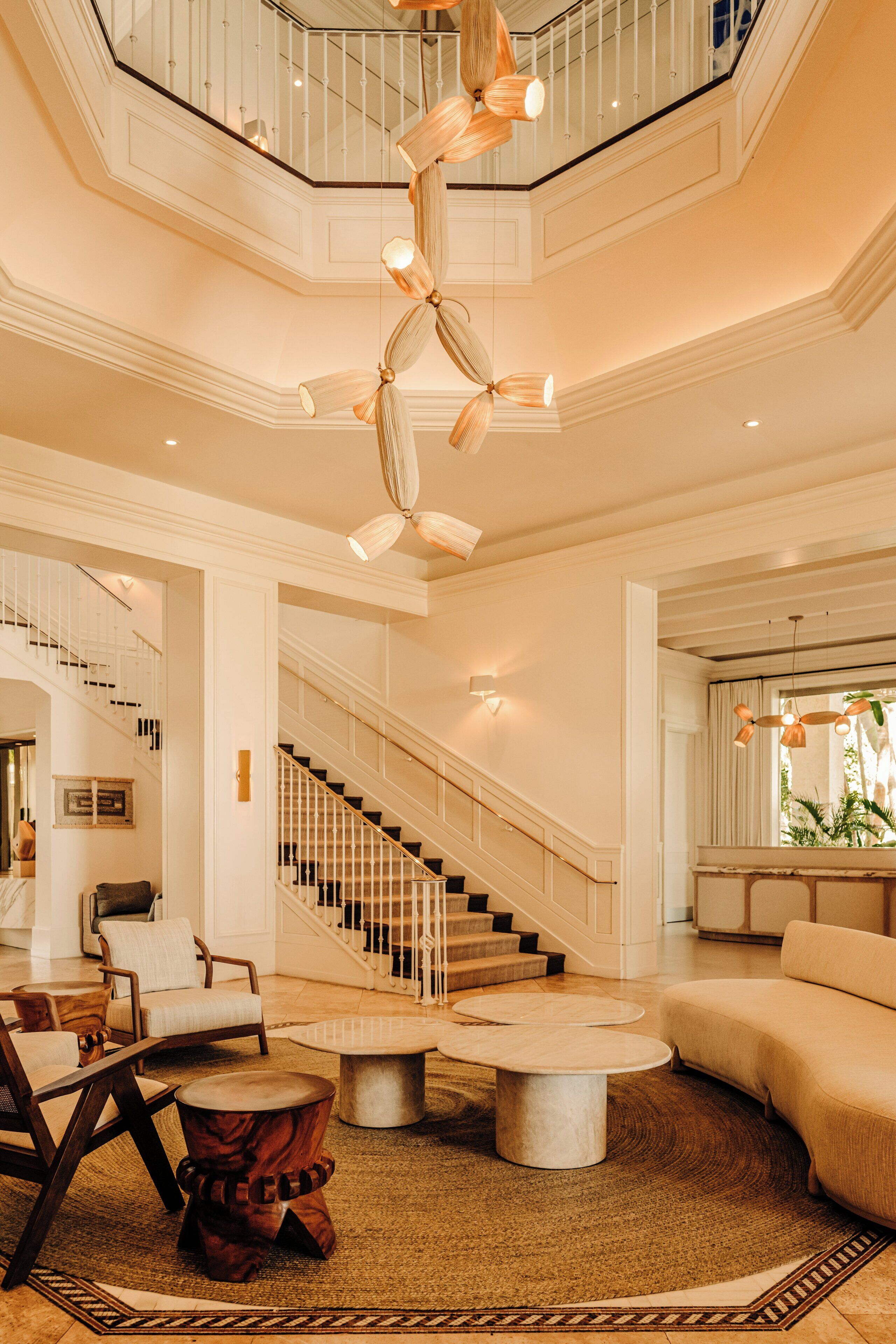 A spacious lobby with a grand staircase, a chandelier, and a seating area with round tables.