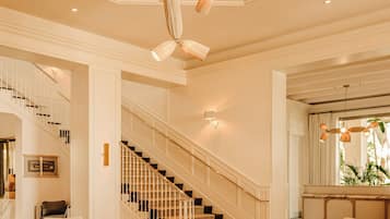 A spacious lobby with a grand staircase, a chandelier, and a seating area with round tables.