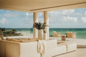 A modern living room with a large white sofa, two wicker chairs, and a view of the ocean. - Four Seasons Resort and Residences Puerto Rico (Río Grande)