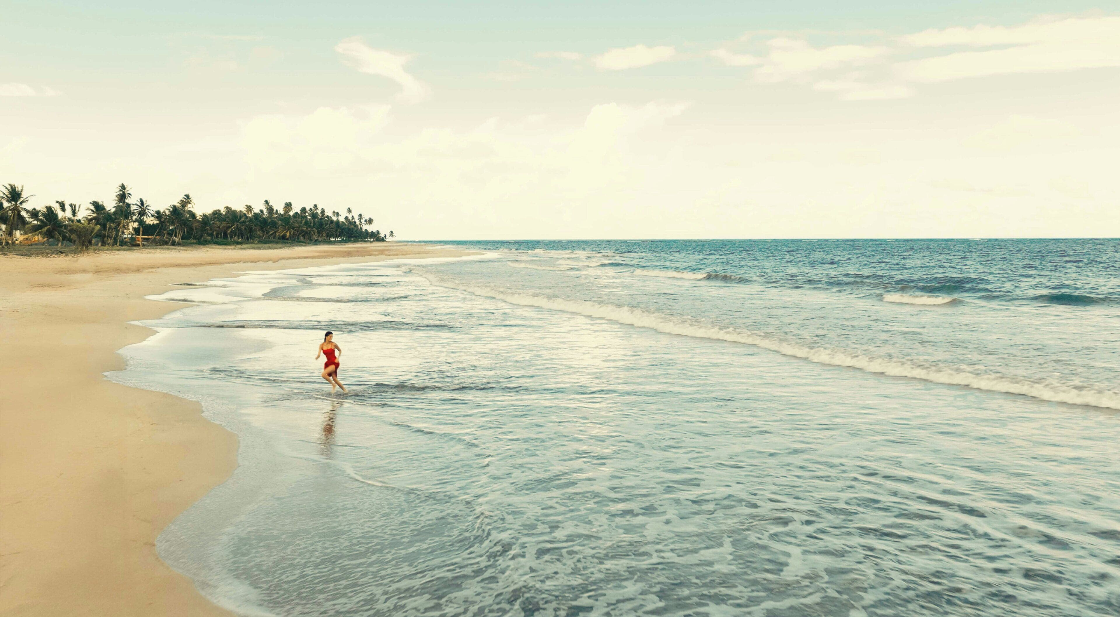 Una playa con una persona en traje de baño caminando por la orilla.