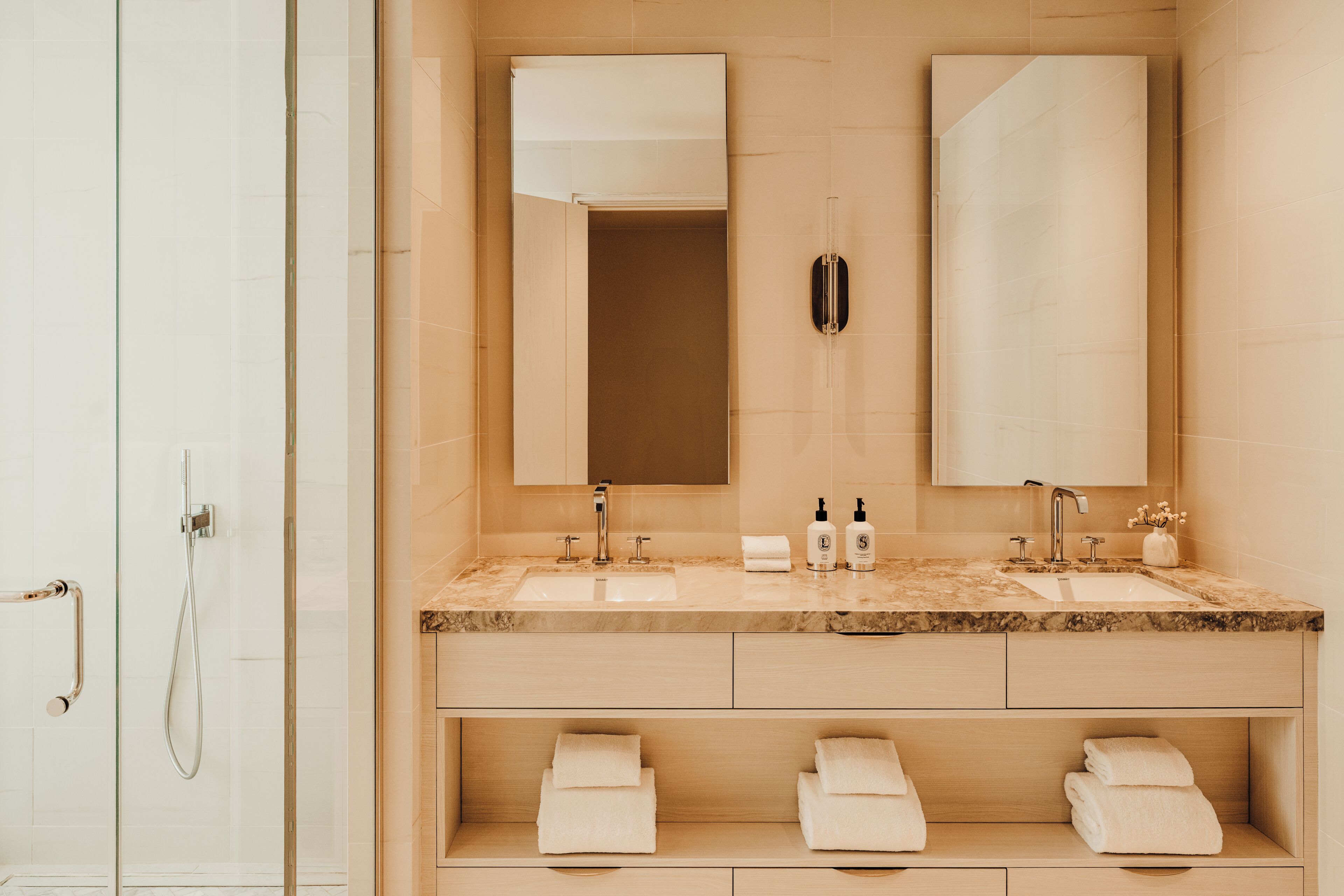 A modern bathroom with two sinks, a shower, and a vanity with storage.