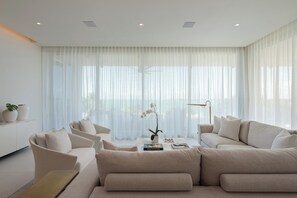 A modern living room with a beige sofa set, a coffee table with books, and a potted orchid.