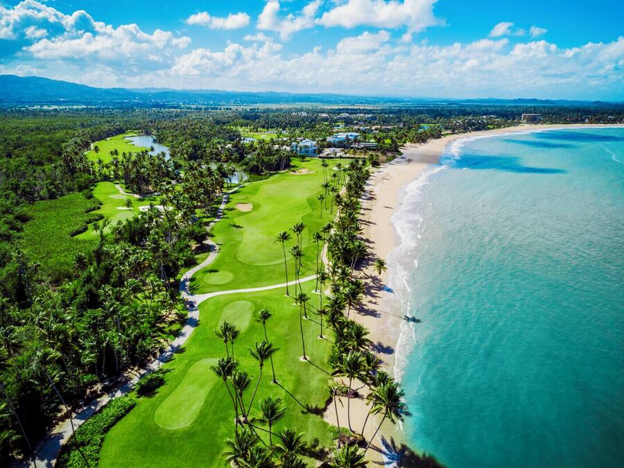 Vue aérienne d’un parcours de golf situé sur la côte, avec une plage et l’océan en arrière-plan.
