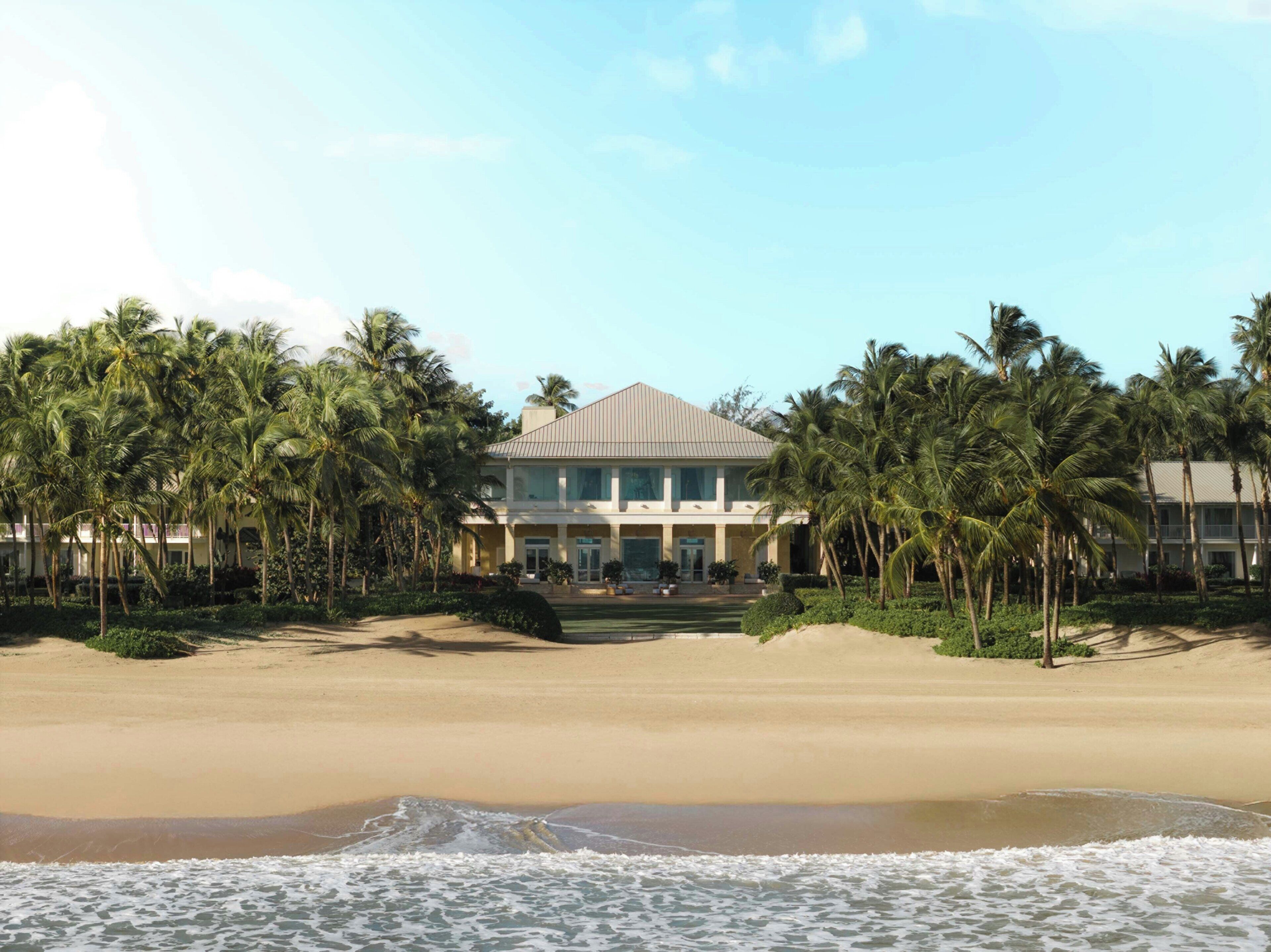 A beachfront hotel with a large building, palm trees, and a sandy beach.