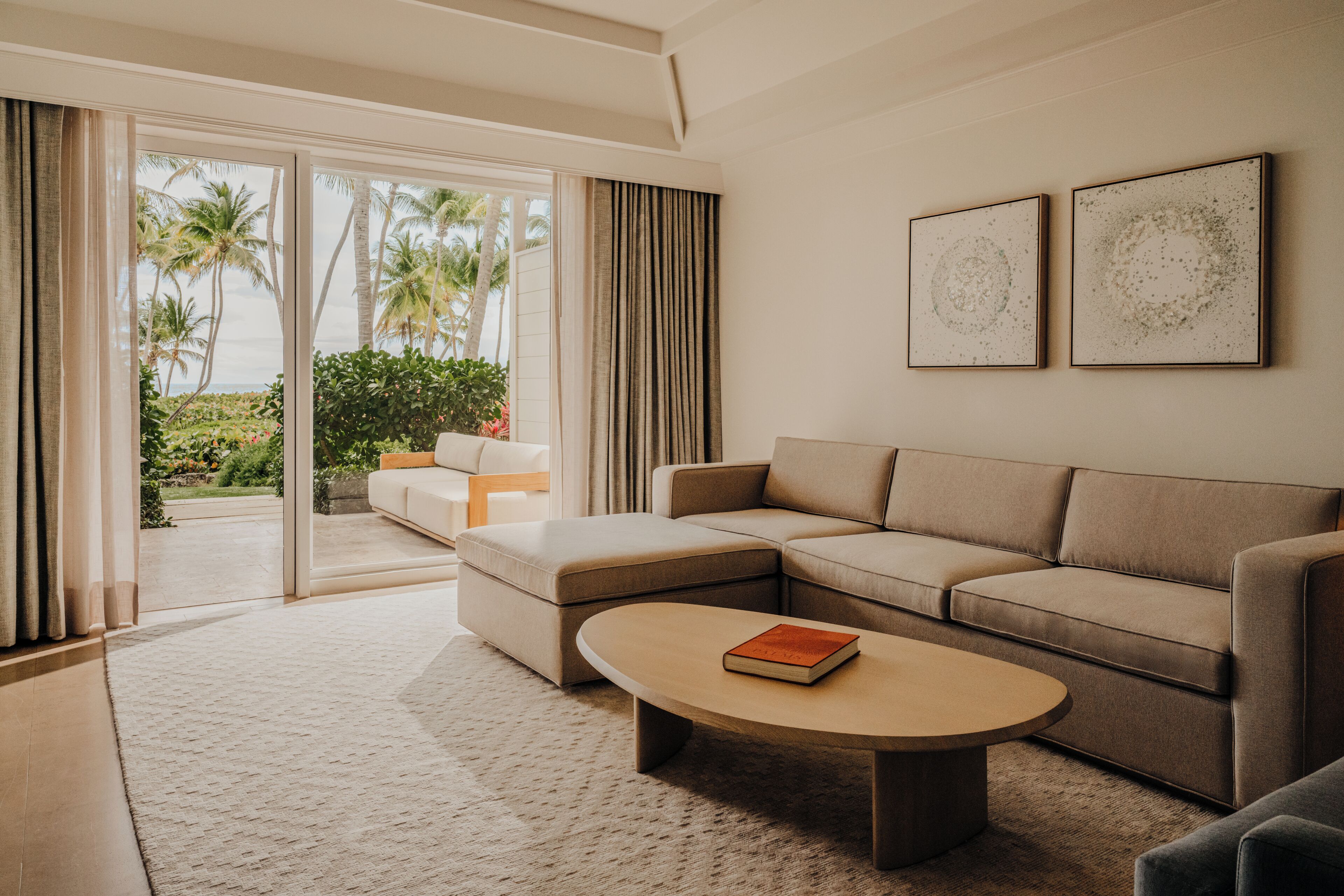 A modern living room with a sectional sofa, a coffee table, and a view of palm trees through large sliding glass doors.