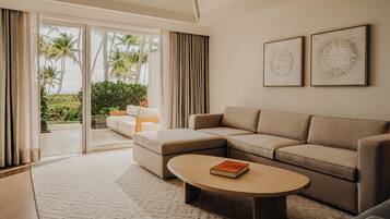A modern living room with a sectional sofa, a coffee table, and a view of palm trees through large sliding glass doors.