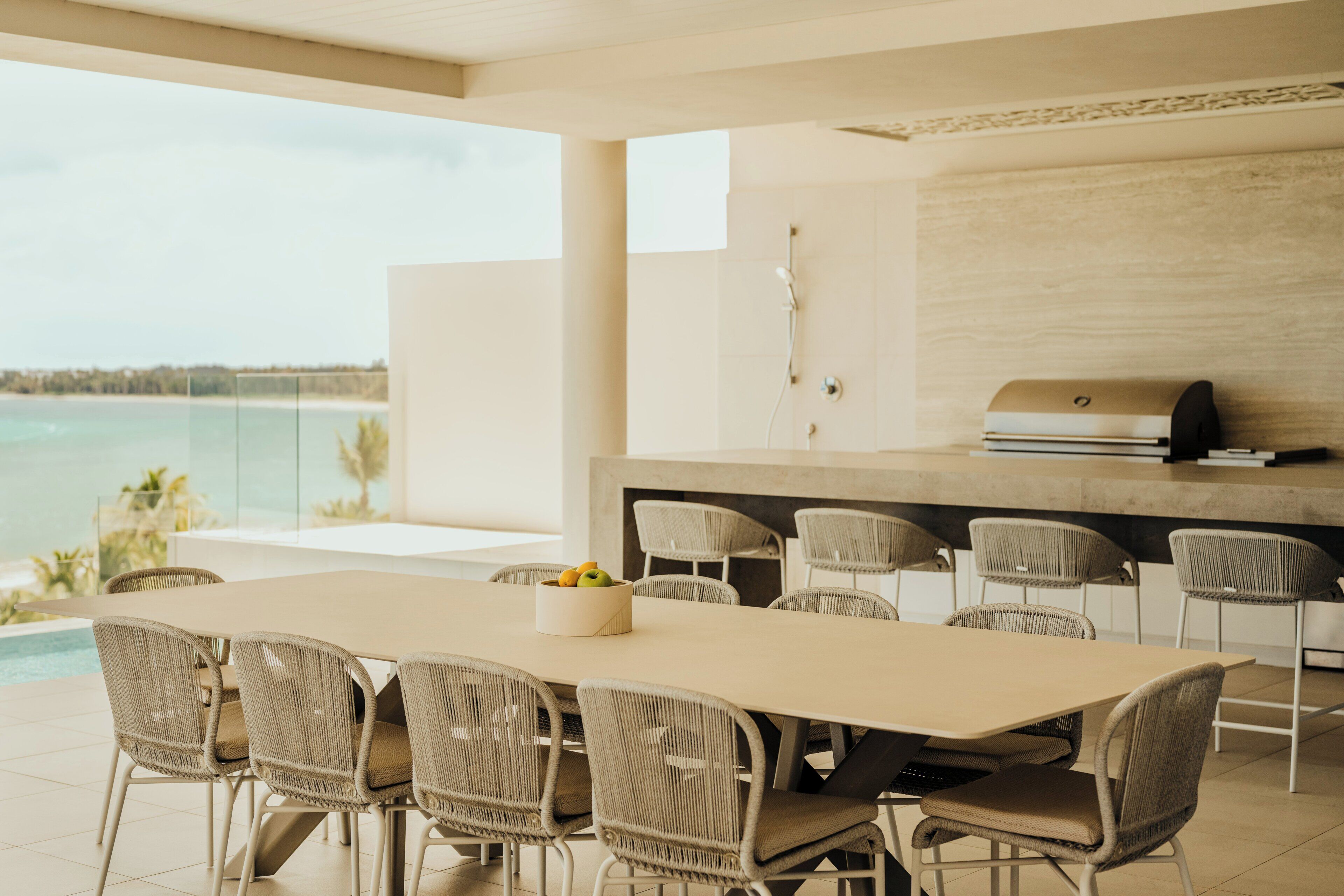 A modern outdoor dining area with a pool view, a built-in grill, and wicker chairs.