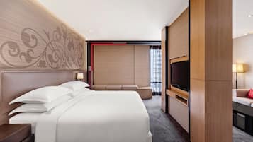 A modern hotel room with a large bed, a TV, and a seating area with a view of the city.