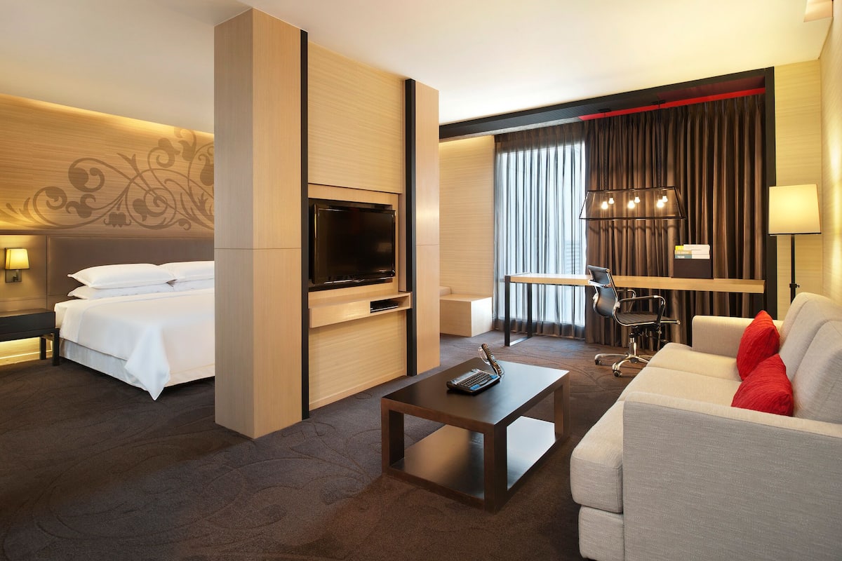 A hotel room with a bed, a TV, a desk with a laptop, a sofa, and a lamp.