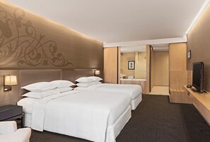 A hotel room with two beds, a desk, a TV, and a bathroom visible through an open door.