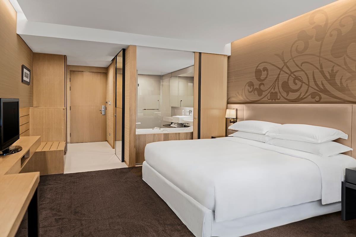 A hotel room with a bed, a desk, a TV, a bathroom, and a mirror.