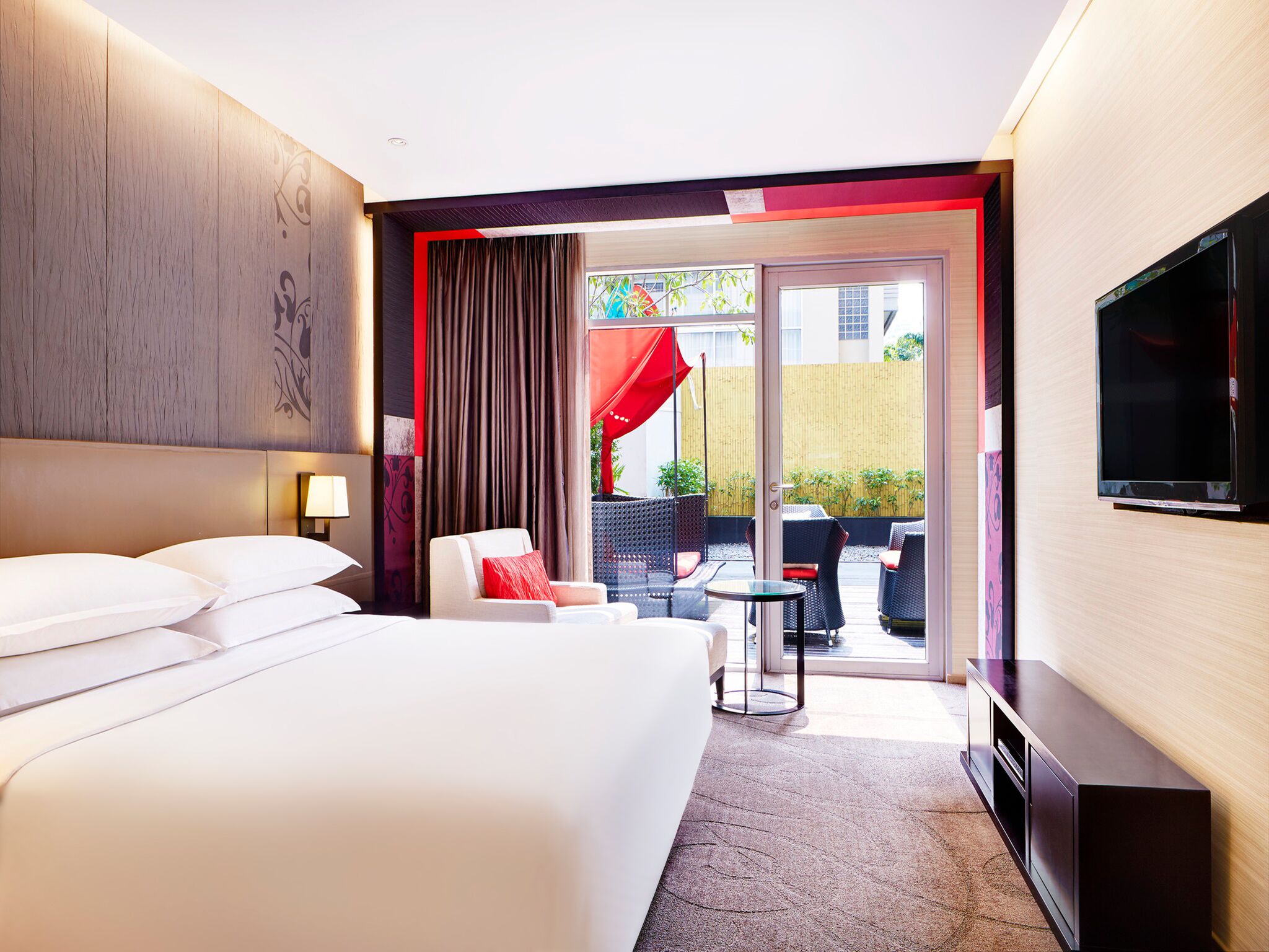 A hotel room with a large bed, a TV, a seating area with a table and chairs, and a view of the outside.