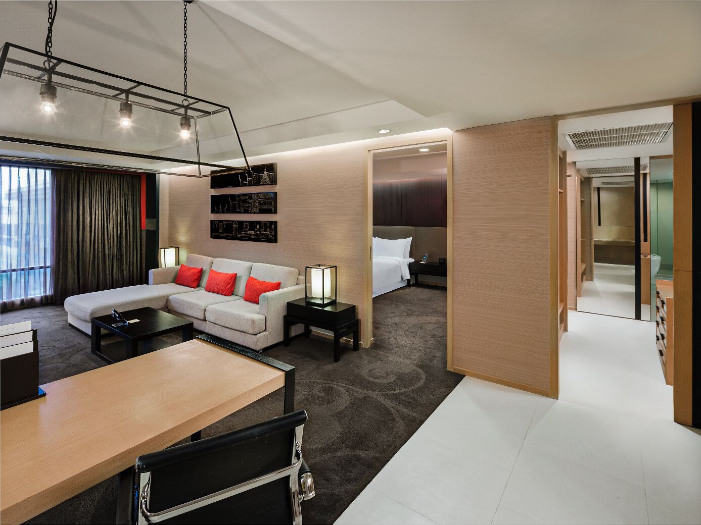 A modern hotel room with a sofa, a desk, a bed, and a bathroom visible through an open door.