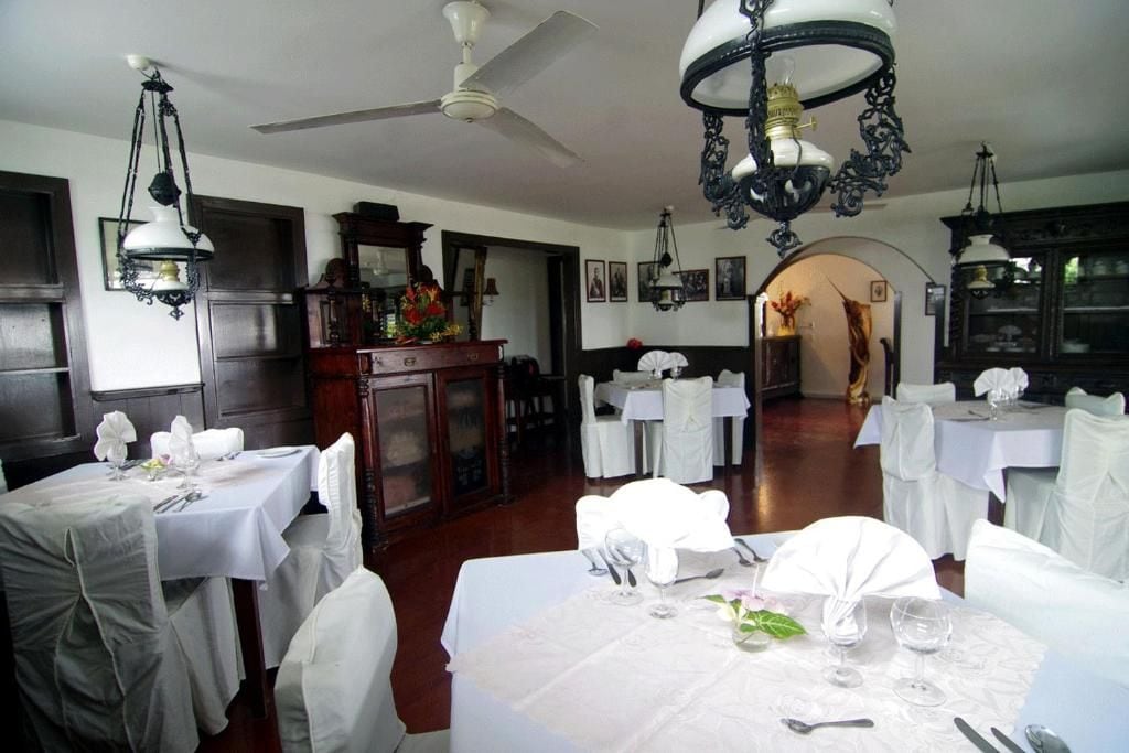 A dining area with tables set for service, a ceiling fan, and a chandelier.