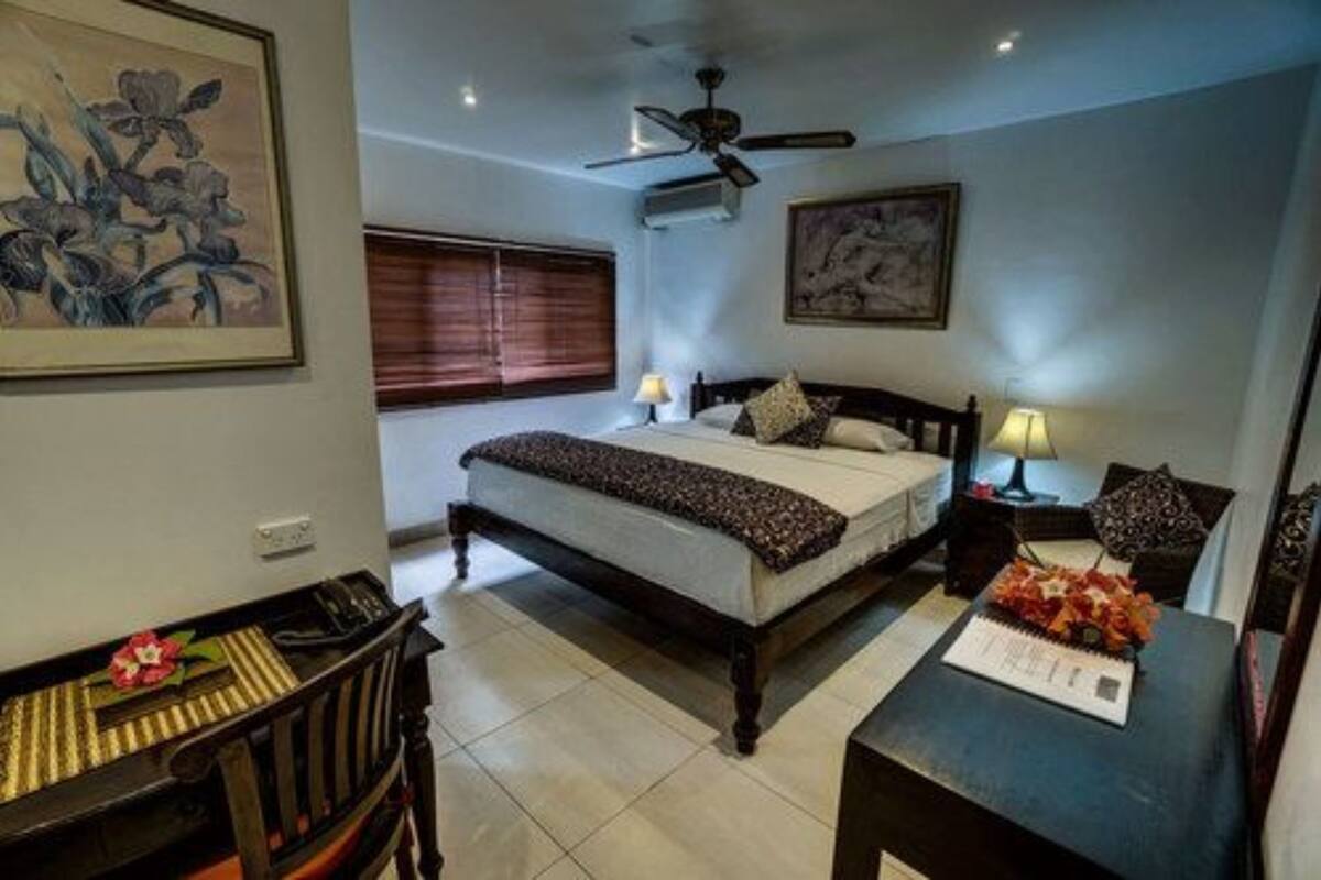 A bedroom with a bed, a desk, a chair, a ceiling fan, and artwork on the walls.