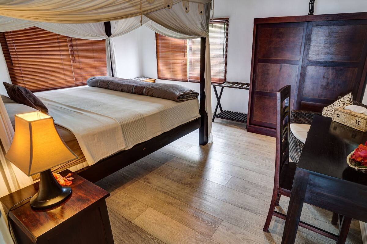 A bedroom with a bed, bedside table, lamp, and a small table with a bowl of flowers.