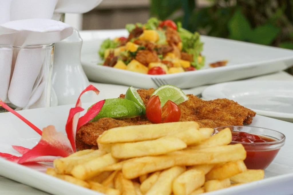 A meal consisting of a breaded cutlet, fries, and a salad with tomatoes and mangoes.