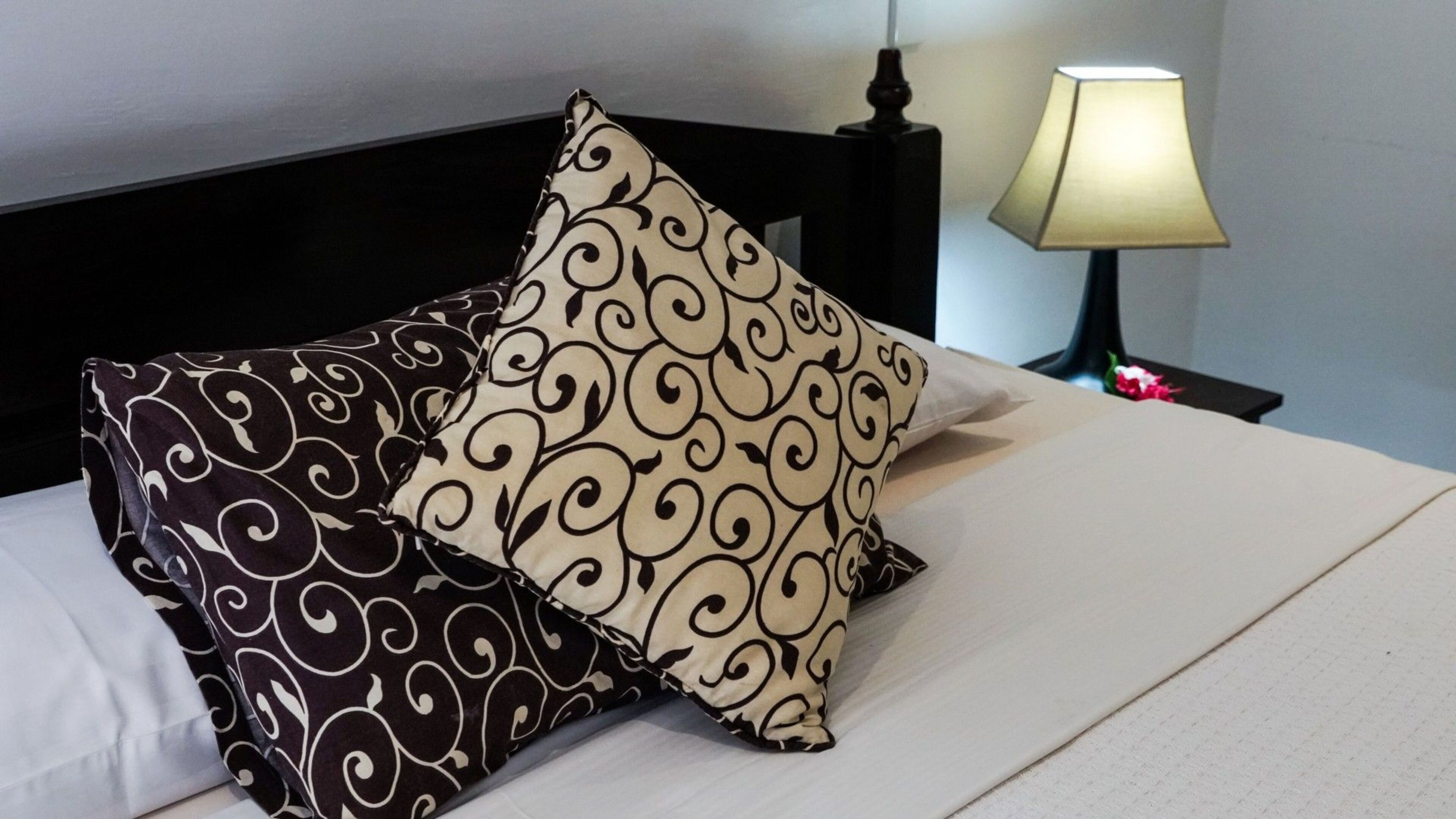 A bed with two patterned pillows and a bedside lamp.
