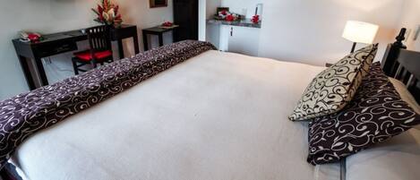 A neatly made bed with patterned bedding, a desk with a chair, a television, and a small cabinet.