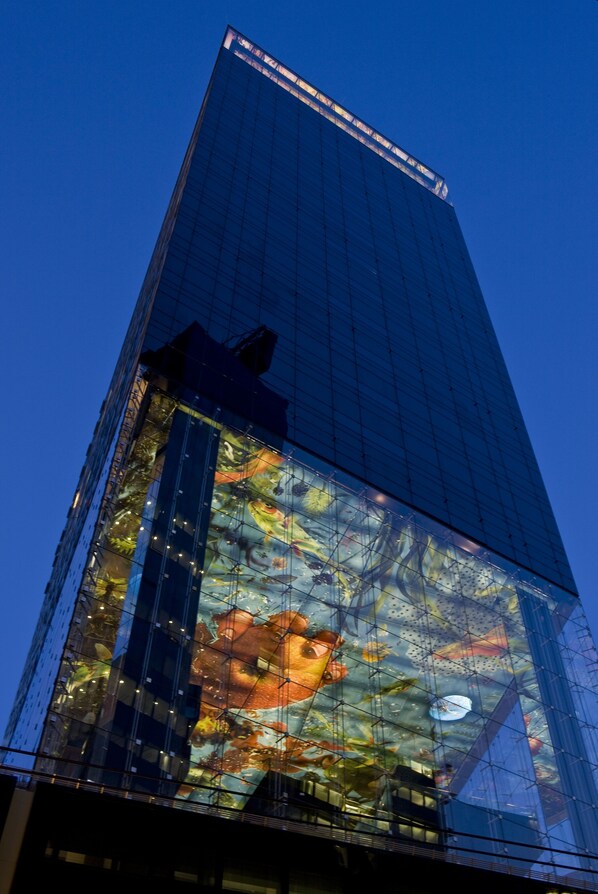 Un edificio alto de vidrio con una gran pantalla digital en la base.