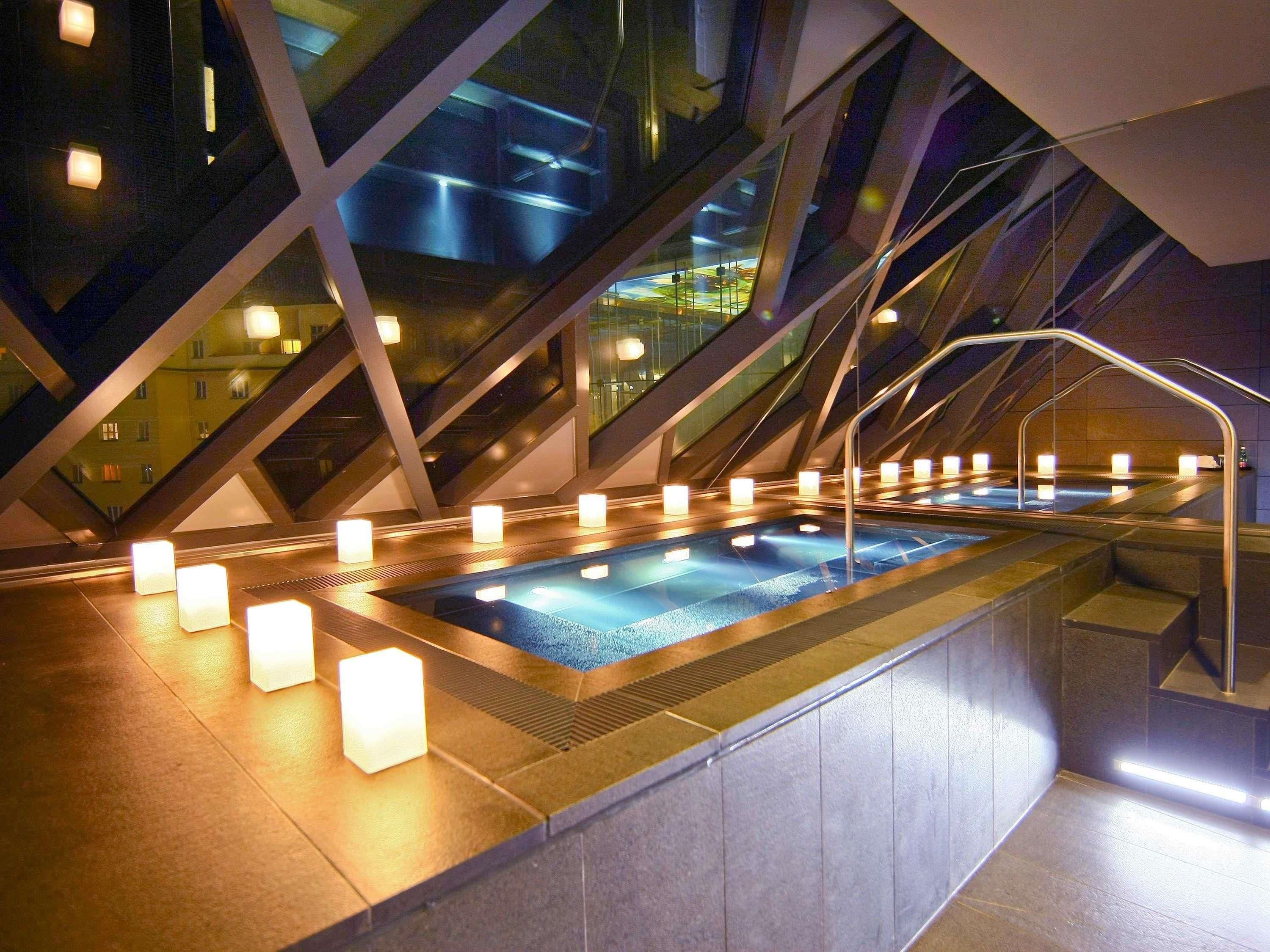 Piscina interior moderna com grades de vidro geométricas e luzes cúbicas iluminadas.