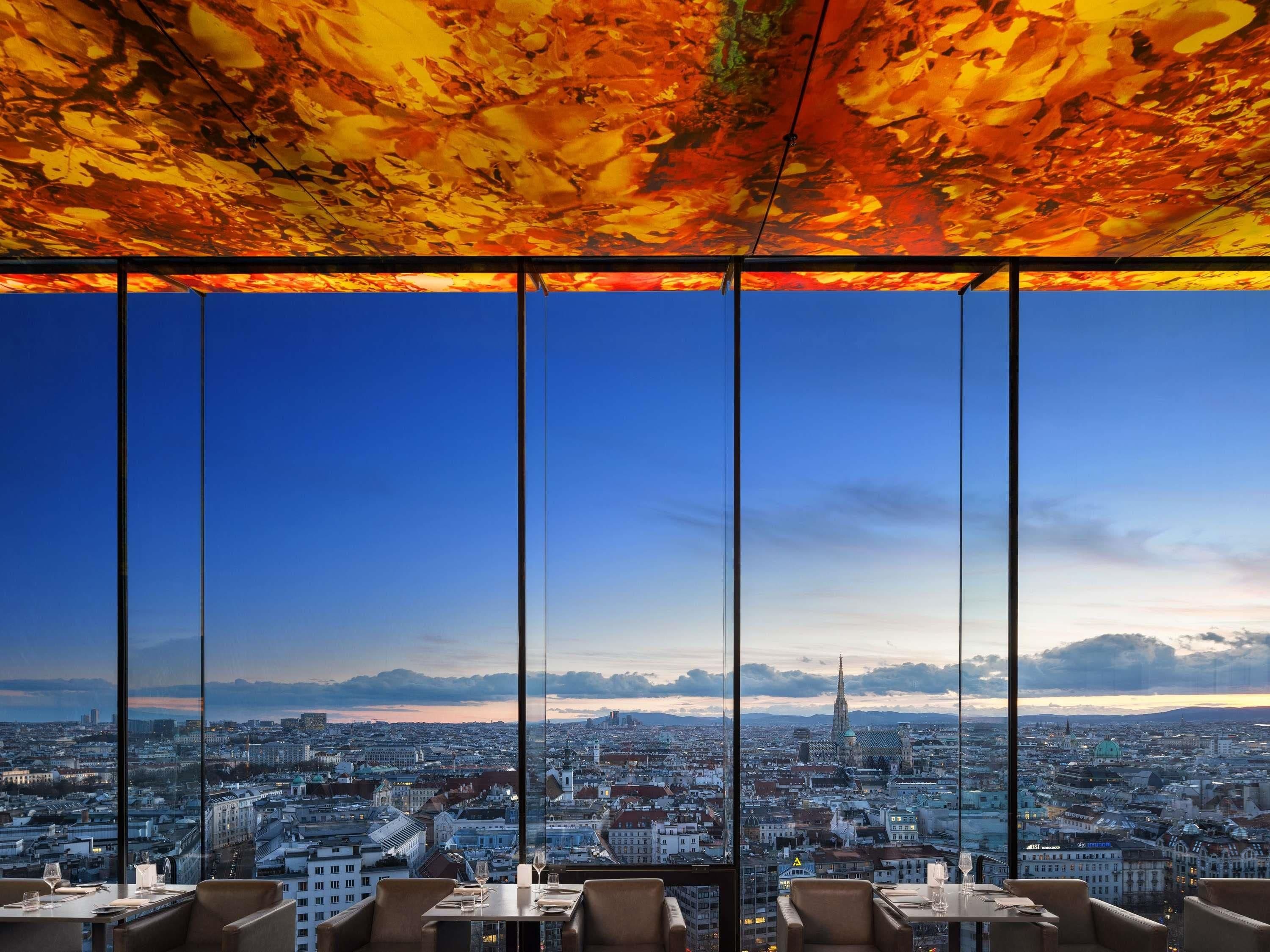 A high-rise restaurant with a panoramic city view, large windows, and a modern interior design.