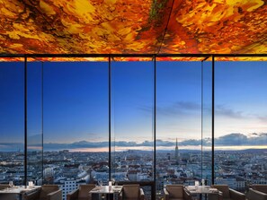 A high-rise restaurant with a panoramic city view, large windows, and a modern interior design.