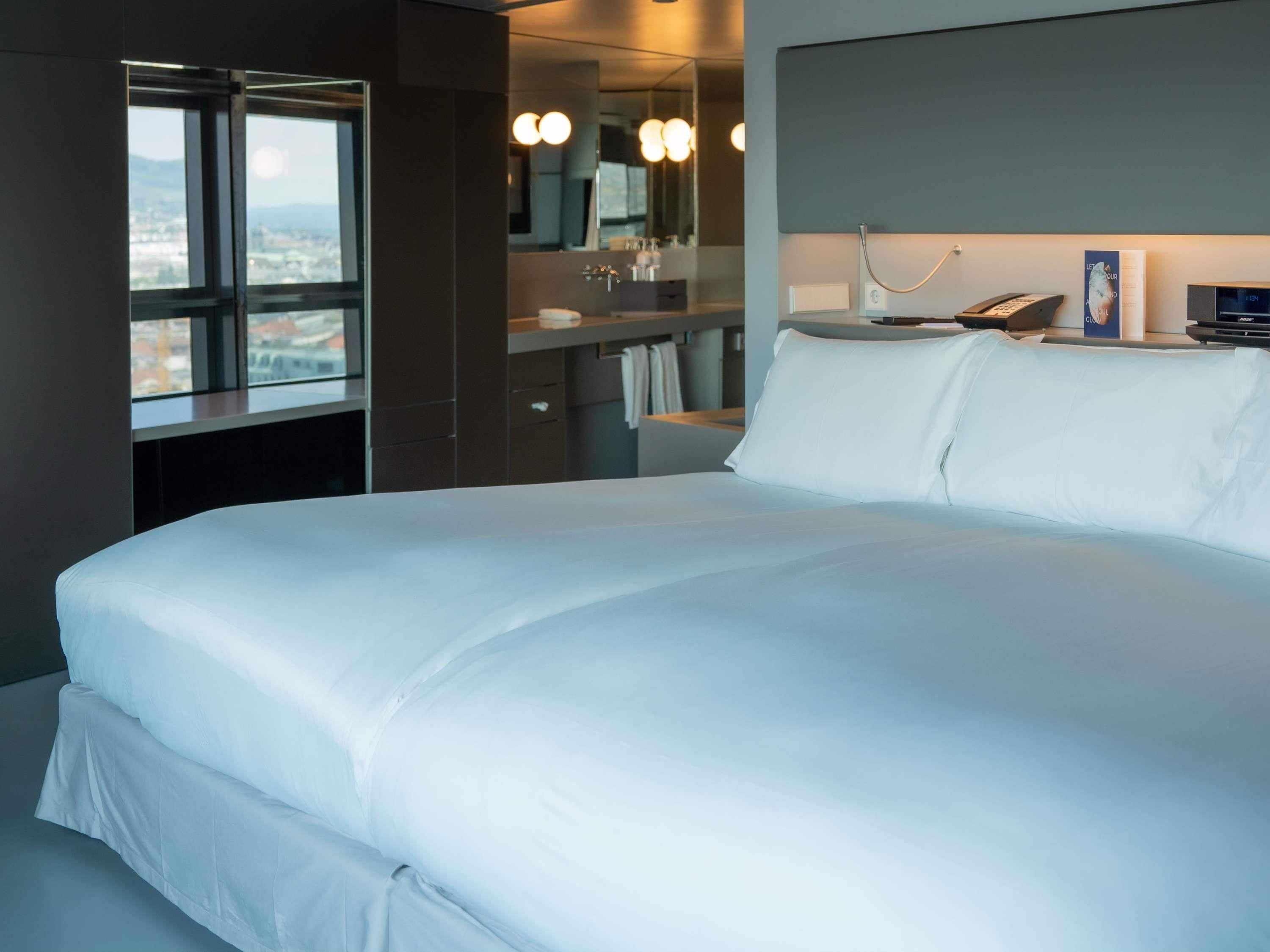Ein modernes Hotelzimmer mit einem großen Bett, einem Badezimmer mit Spiegel und Blick auf die Stadt.