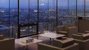 Un salón moderno con amplios ventanales que ofrecen vistas a la ciudad, una mesa de centro y asientos cómodos.