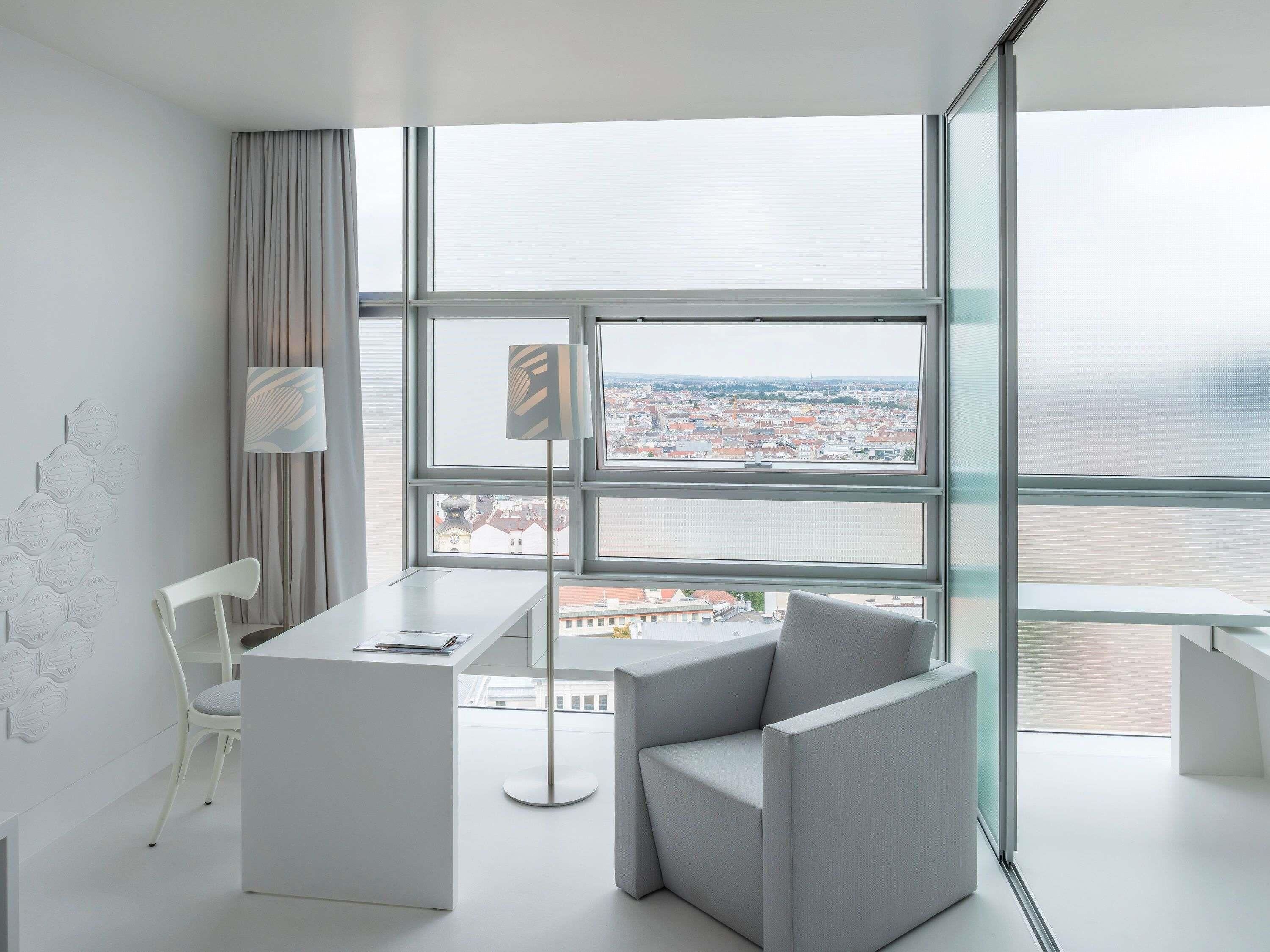 Quarto moderno com uma janela grande, uma escrivaninha, duas cadeiras e um abajur.