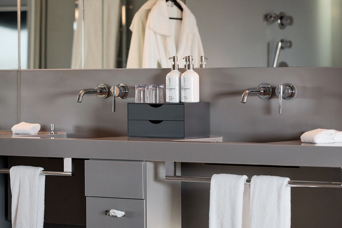 Un baño moderno con un espejo grande, dos lavamanos y un perchero para toallas.
